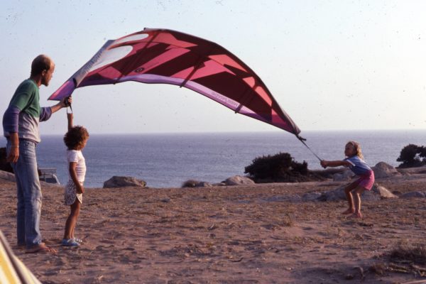Father holding an old windsurfing sail with his two kids